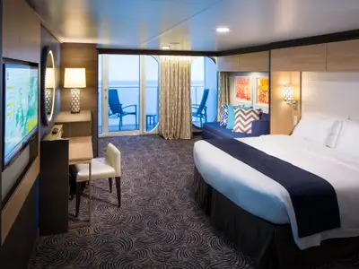 Moderne Kabine an Bord der Anthem of the Seas mit großem Bett, blauem Sofa und Schreibtisch. Der Balkon bietet direkten Meerblick auf die offene See.