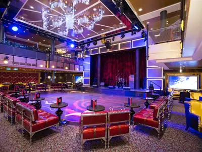 Die 270°-Lounge auf der Anthem of the Seas: Bühne, Instrumente, Tanzfläche, rote Lounge-Sitzgelegenheiten. Kronleuchter und obere Galerie sind zu sehen.