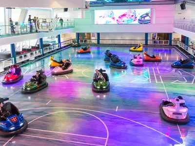 Auf der Anthem of the Seas fahren Passagiere Bumper Cars auf einem farbigen Feld. Zuschauer beobachten von der Galerie. Ein großer Bildschirm zeigt Grafiken.