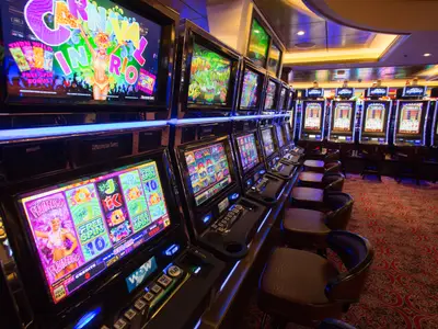 Leuchtende Spielautomaten-Reihe mit bunten Grafiken im Casino der Anthem of the Seas. Gepolsterte Hocker davor und weitere Maschinen im Hintergrund.