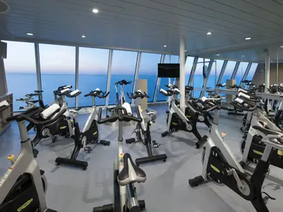 Blick in den modernen Fitnessraum für Spinning-Kurse an Bord der Anthem of the Seas. Zahlreiche Fahrräder stehen bereit, dahinter große Fenster mit weitem Meerblick auf das Meer.