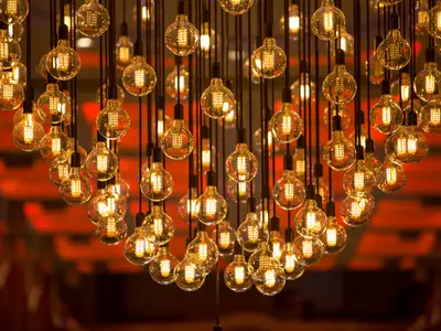 Eine Kunstinstallation aus vielen hängenden Edison-Glühbirnen, die warmes, goldenes Licht in einem Innenraum ausstrahlen. Ihre LED-Filamente sind klar erkennbar.