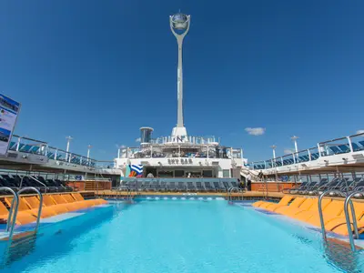Blick auf das Hauptpooldeck der Anthem of the Seas. Der große Pool mit orangefarbenen Liegen im Vordergrund, dahinter die SKY BAR und der markante North Star.