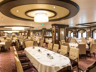 Der Hauptspeisesaal auf der Anthem of the Seas. Er ist mit vielen gedeckten Tischen, bequemen Stühlen, Kronleuchtern und aufwendiger Inneneinrichtung gestaltet.