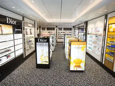 Blick in den Duty-Free-Shop der Anthem of the Seas. Zu sehen sind helle Gänge mit Regalen voller Parfums und Kosmetikprodukte internationaler Marken wie Dior und L'Occitane.