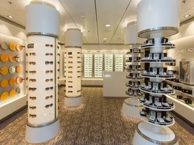 Innenansicht eines hell beleuchteten Ladens an Bord der Anthem of the Seas, mit runden Säulen voller Sonnenbrillen und drehbaren Uhrendisplays.