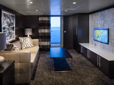 Geräumiges Wohnzimmer einer Kabine auf der Anthem of the Seas mit Sofa, Couchtisch, TV-Bereich und Balkon mit Meerblick.