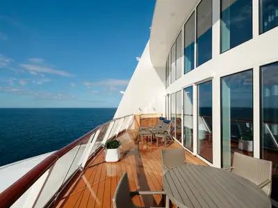 Der weitläufige Balkon einer Suite der Anthem of the Seas zeigt Outdoor-Möbel, hohe Glasfronten und das offene blaue Meer unter klarem Himmel.