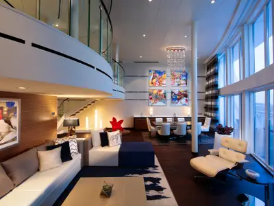 Die luxuriöse, zweistöckige Suite auf der Anthem of the Seas zeigt einen modernen Wohn- und Essbereich mit stilvollen Möbeln, Kunstwerken und großen Fenstern.
