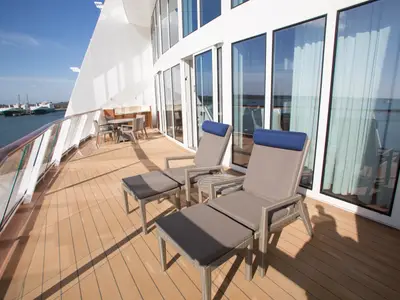 Ein geräumiger Balkon der Anthem of the Seas mit zwei Liegestühlen, einem Esstisch und Blick auf das Meer sowie andere Schiffe im Hafen.