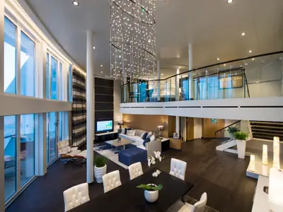 Großzügige, moderne zweistöckige Suite auf der Anthem of the Seas. Unten Wohn- und Essbereich, oben Schlafbereich. Große Fenster, dunkler Holzboden, heller Essbereich, Kronleuchter.