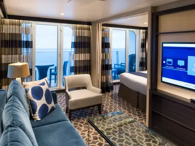 Innenansicht einer Suite auf der Anthem of the Seas. Der Wohnbereich mit blauem Sofa und der Schlafbereich bieten Zugang zu zwei Balkonen mit Meerblick.