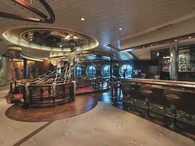 Innenansicht der Schiffs-Lounge auf der Explorer of the Seas. Im Zentrum ein großes, maritimes Holzmodell. Rechts befindet sich eine lange Bar mit Hockern und Flaschen. Runde Fenster bieten Ausblick.