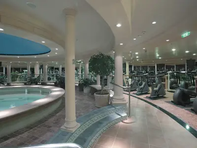 Blick auf den gut ausgestatteten Fitness- und Spa-Bereich an Bord der Explorer of the Seas. Im Vordergrund ein runder Whirlpool, dahinter ein großer Trainingsbereich mit vielen Fitnessgeräten.