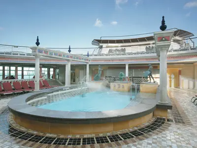 Der Solarium Poolbereich der Explorer of the Seas zeigt ein Becken mit Fontänen, Statuen, roten Liegen und Säulen unter blauem Himmel.