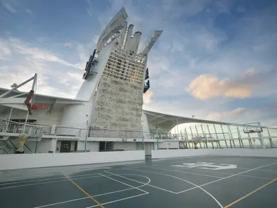 Auf dem Sportdeck der Explorer of the Seas sind ein Basketballfeld mit zwei Körben und eine Kletterwand am Schornstein zu sehen. Der blaue Himmel ist leicht bewölkt.