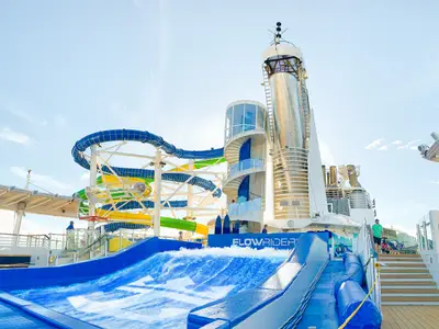 Das Oberdeck der Freedom of the Seas zeigt FlowRider Surfsimulator und bunte Wasserrutschen. Ein hoher Turm mit Wendeltreppe ist sichtbar. Blauer Himmel, wenige Personen.