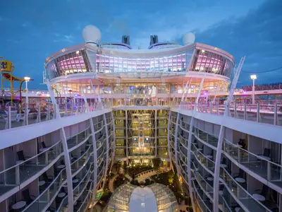 Dämmerungsansicht der Harmony of the Seas von oben. Das beleuchtete Central Park Deck mit Balkonen, Gärten und Glasstrukturen ist zu sehen. Oben links ein Wasserpark.
