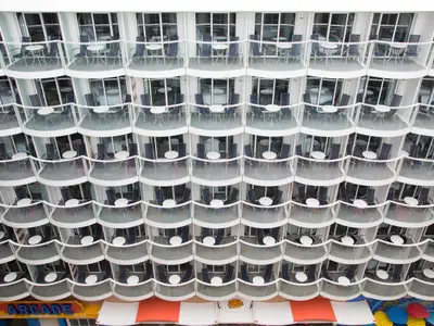 Blick von oben auf die Wellenform der Kabinenbalkone der Harmony of the Seas. Viele Balkone mit Tisch und Stühlen sind zu sehen, unten ein Arkaden-Schild.