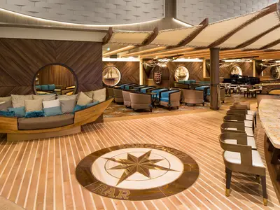 Die Schooner Bar der Harmony of the Seas mit nautischer Einrichtung, einer Boots-Sitzbank, einer Kompassrose im Holzboden, Sitzgruppen und einem Flügel.