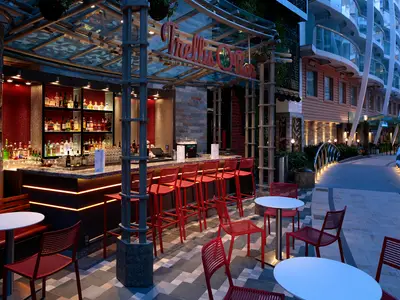 Abendliche Ansicht der Trellis Bar im Central Park der Harmony of the Seas. Die beleuchtete Bar mit roten Sitzgelegenheiten, einem Spazierweg und den Schiffskabinen im Hintergrund.