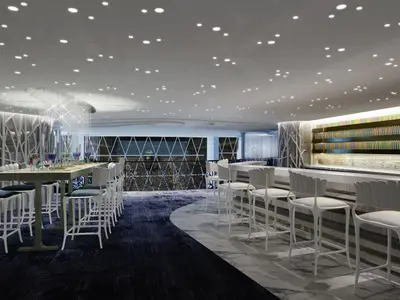 Moderne Bar-Lounge mit Tischen und Stühlen. Rechts lange Theke mit bunten Flaschen. Decke hat Lichter und Lichtskulptur. Boden aus Teppich und Marmor.