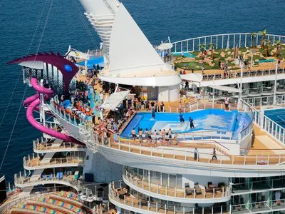 Luftaufnahme der oberen Decks der Harmony of the Seas. Zu sehen sind der lila Rutschenkomplex Ultimate Abyss, der FlowRider Surfsimulator mit Surfern und eine Minigolfanlage mit Palmen. Viele Passagiere beleben die Decks.