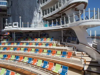 Sonniger Blick auf das Open-Air-Amphitheater mit bunten Stühlen auf dem Deck der Harmony of the Seas. Im Hintergrund sind eine Kletterwand und obere Decks sichtbar. Das Meer ist am Horizont erkennbar.