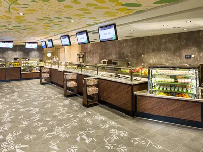 Buffetbereich auf der Harmony of the Seas. Holztheken, Marmorplatten und digitale Menüanzeigen. Decke mit Blättermuster, gemusterter Boden.