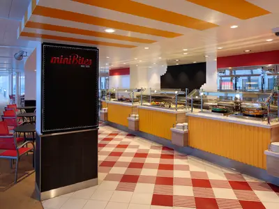 Buffetbereich an Bord der Harmony of the Seas. Gelbe Theken mit Speisen, ein rot-weiß karierter Boden und orange-weiß gestreifte Decke. Tische und rote Stühle im Hintergrund.