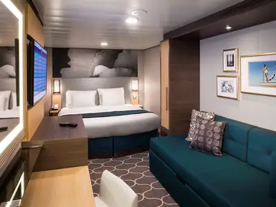 Eine moderne Innenkabine der Harmony of the Seas mit Doppelbett, blauem Sofa, Schreibtisch mit TV und Spiegel. Helle, funktionale Einrichtung.