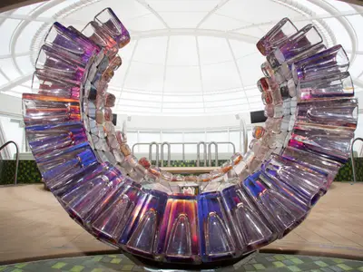 U-förmige Glaskunstinstallation auf der Harmony of the Seas. Schimmernde Glasstücke reflektieren Farben unter einer Glaskuppel und Fenstern.