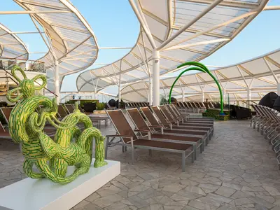 Das Sonnendeck der Harmony of the Seas: Eine grüne Skulptur, viele Liegestühle, ein gewelltes Dach und heller Boden.