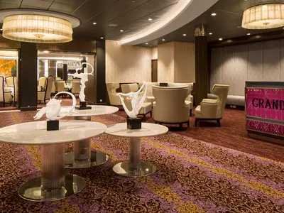 Harmony of the Seas: Elegante Lounge. Weiße Skulpturen auf Tischen. Bequeme Sitzgruppen. Empfang Grande Restaurant. Gemusterter Teppich. Elegante Deckenleuchten.