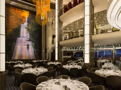 Elegantes, mehrstöckiges Restaurant an Bord der Harmony of the Seas mit vielen gedeckten Tischen, großem Wandgemälde und Kronleuchter.