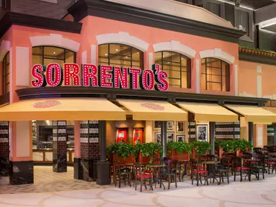 Das italienische Restaurant Sorrento's auf der Harmony of the Seas mit leuchtendem Schriftzug und mehreren Sitzbereichen im Freien unter gelben Markisen.