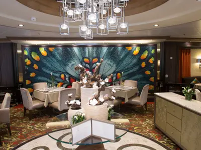 Restaurant der Harmony of the Seas: Große Wand mit Schmetterlingsmosaik, Tische, Stühle, Blumendeko und moderner Kronleuchter.