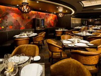 Ein elegantes Restaurant an Bord der Harmony of the Seas mit gedeckten Tischen, bequemen Ledersesseln und einer auffälligen Wandgestaltung mit roten und orangefarbenen Kreisen.