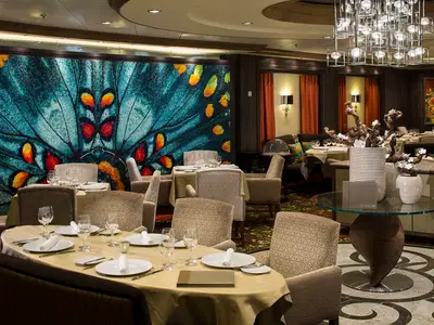 Restaurant auf der Harmony of the Seas mit großem Schmetterlings-Mosaik an der Wand. Elegant gedeckte Tische, gepolsterte Stühle, Kronleuchter, stilvolles Ambiente.