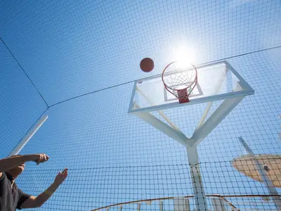 Basketball auf der Harmony of the Seas: Eine Person wirft den Ball auf den Korb. Ein Schutznetz spannt sich über das Sportdeck unter blauem Himmel mit heller Sonne.