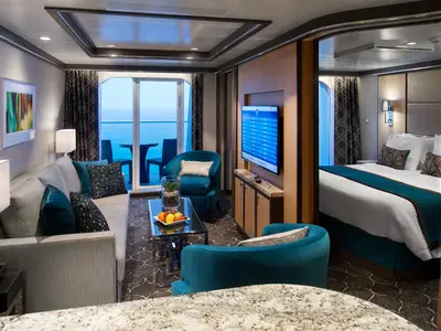 Innenansicht einer luxuriösen Suite auf der Harmony of the Seas. Die Aufnahme zeigt den Wohnbereich mit Sofa, TV und Meerblickbalkon sowie einen Teil des angrenzenden Schlafzimmers.