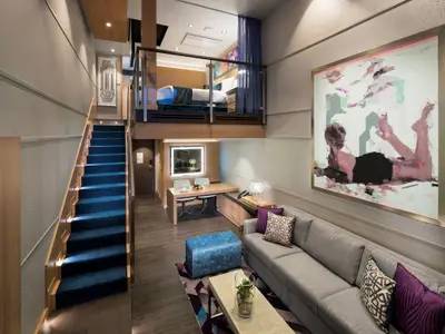 Geräumige zweistöckige Suite an Bord der Harmony of the Seas. Unten ein Wohnbereich mit Sofa, Esstisch und Kunst, oben ein Schlafzimmer im Loft, verbunden durch eine beleuchtete Treppe.