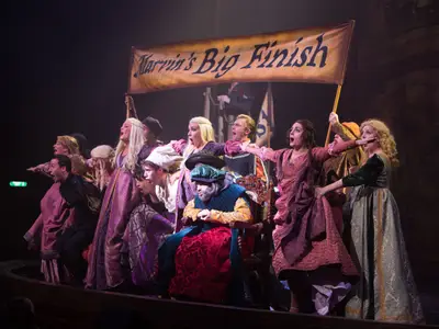 Szene einer Theateraufführung "Marvin's Big Finish" an Bord der Harmony of the Seas. Zahlreiche Darsteller in historischen Kostümen singen auf einer Bühne, ein Banner ist sichtbar.