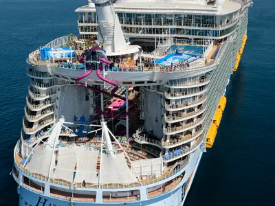 Das Heck der Harmony of the Seas von oben zeigt bunte Wasserrutschen, Kletterwände, einen Surfsimulator, Balkonkabinen und ein Freilufttheater auf blauem Meer.