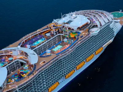 Luftaufnahme der Harmony of the Seas bei Dämmerung, die mehrere Decks mit Pools, Wasserrutschen und Balkonkabinen zeigt, umgeben von dunklem Meer.