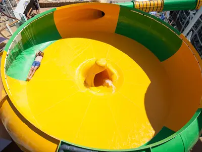 Ein Mann liegt auf dem Rücken in einer gelb-grünen Wasserrutsche an Bord der Harmony of the Seas. Wasser fließt zum zentralen Abfluss. Teile des Schiffsdecks sind im Hintergrund zu sehen.