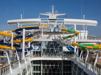 Nahaufnahme des Hecks der Harmony of the Seas, die bunte Wasserrutschen, Freidecks und einen Teil der oberen Brückenstruktur unter klarem Himmel zeigt. Die Rutschen sind gelb, blau und grün.