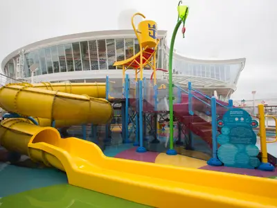 Kinder-Wasserpark auf der Harmony of the Seas: gelbe Rutschen, großer Kippeimer mit Logo, bunte Spielgeräte, Treppen.