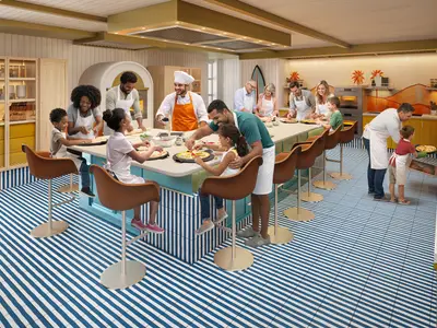 Pizza-Kochkurs auf der hero of the seas: Familien und Gäste belegen Pizzen an der Kücheninsel. Ein Koch hilft. Ein Kind schiebt Pizza in den Ofen. Blau-weiß gestreifter Boden.