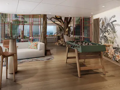 Innenansicht eines Freizeitbereichs auf der hero of the seas mit Schachbrett-Tisch, Kicker, Sofa und großem Meerblick. Eine Wand ist mit einem tropischen Muster bemalt.